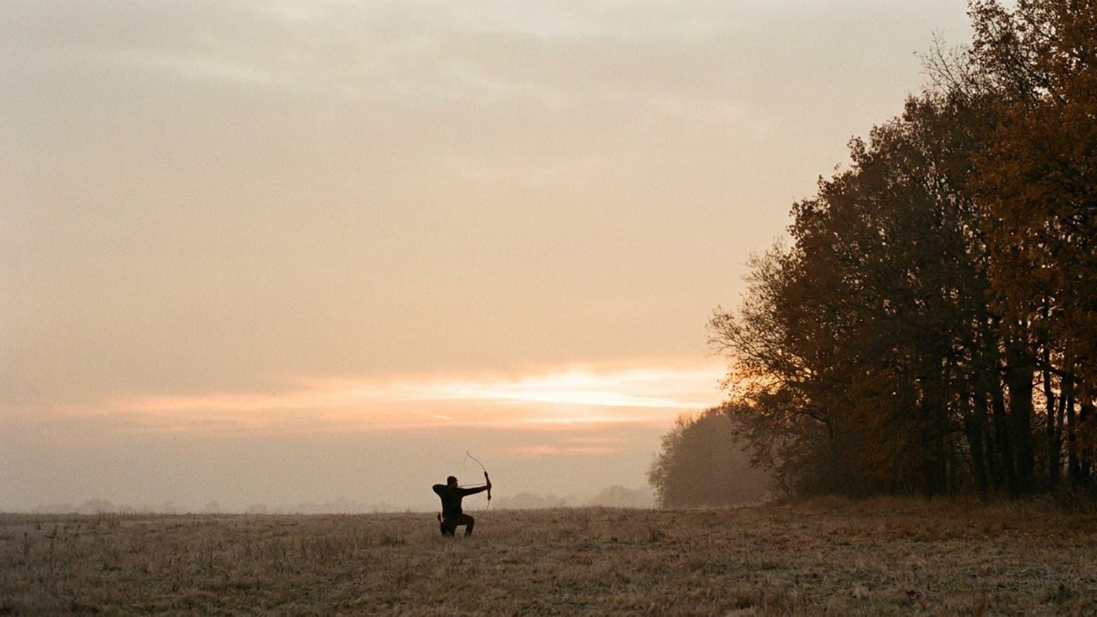 A distant archer at full draw silhouetted against a dawn sky at a field edge
