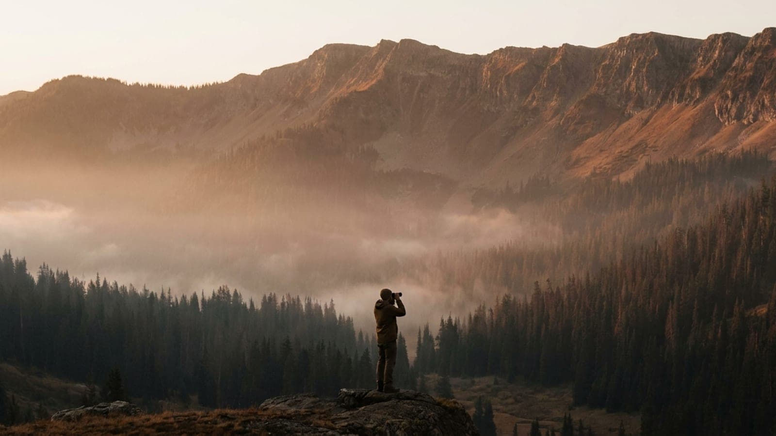 A hunter glassing a misted mountain valley at dawn